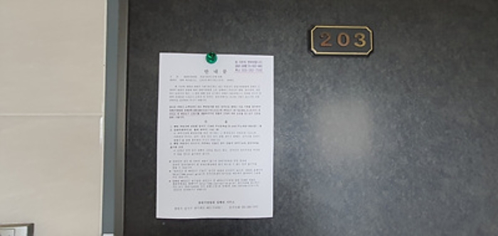 203호의 출입문에 부동산경매 사건에 대한 안내문 게시(8/6)