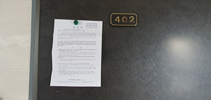 402호의 출입문에 부동산경매 사건에 대한 안내문 게시(8/6)